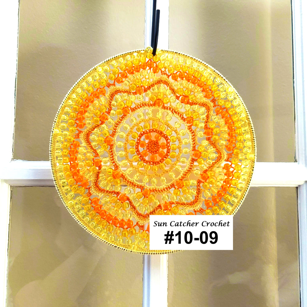 Sun catcher crochet item with a yellow and orange pattern, hanging on a window.