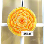 Sun catcher crochet item with a yellow and orange pattern, hanging on a window.