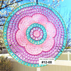 Decorative sun catcher with pink and blue spiral design hanging outdoors.