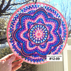 Colorful beaded circular craft held by a hand with a blurred outdoor background