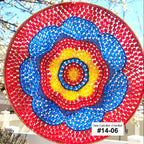 Colorful circular sun catcher with concentric circles of red, blue, and yellow against a blurred outdoor background.