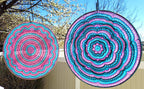 Two colorful circular patterns hanging outdoors with trees and blue sky in the background.