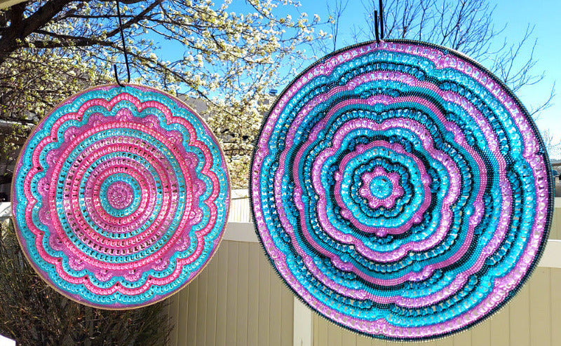 Two colorful circular patterns hanging outdoors with trees and blue sky in the background.