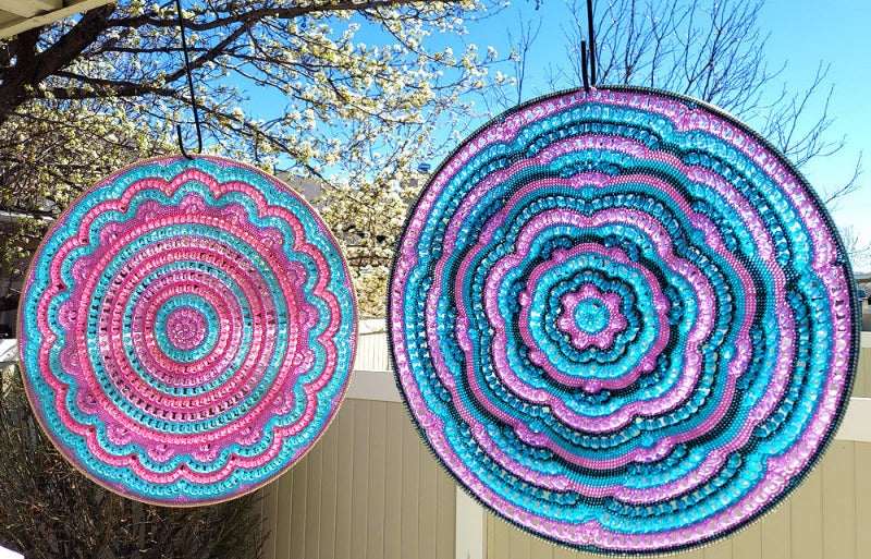 Two colorful circular patterns hanging outdoors with trees and blue sky in the background.