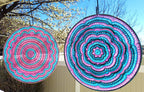 Two colorful circular patterns hanging outdoors with trees and blue sky in the background.