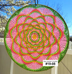 Circular crochet sun catcher with pink, green, and light orange pattern against a blue sky.