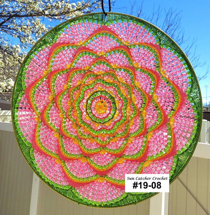 Circular crochet sun catcher with pink, green, and light orange pattern against a blue sky.
