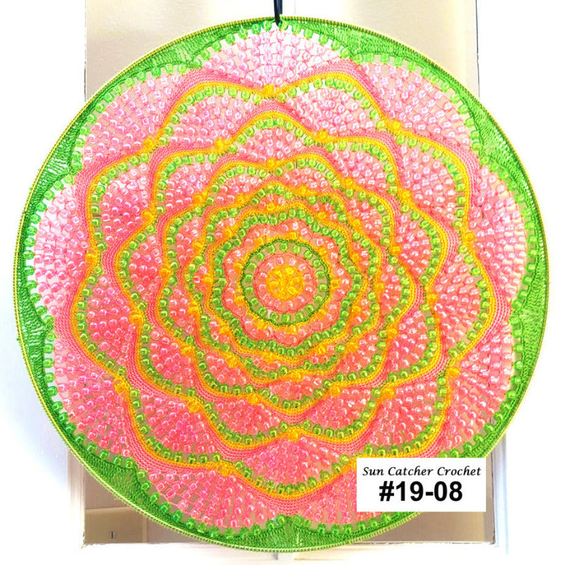 Circular sun catcher crochet item with pink, green, and light orange colors on a white background.