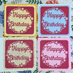 Four 'Happy Birthday' cards in different colors on a floral background