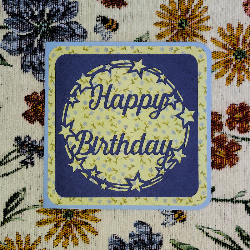Happy Birthday card with decorative text on a floral fabric background