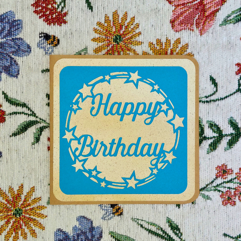 Happy Birthday card with blue background and beige border on floral fabric