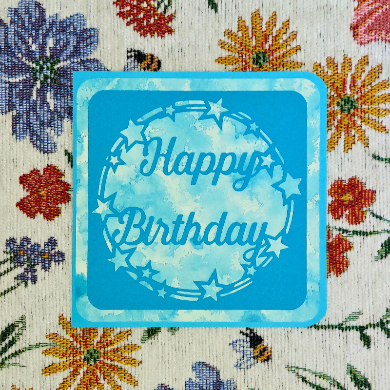 Blue 'Happy Birthday' card on a floral fabric background