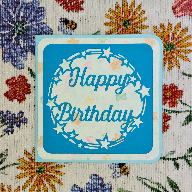 Blue 'Happy Birthday' card with star design on a floral-patterned background