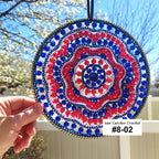 Decorative sun catcher with red, blue, and white pattern held by a hand outdoors.