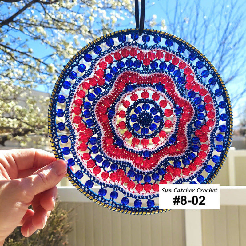 Decorative sun catcher with red, blue, and white pattern held by a hand outdoors.