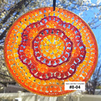 Circular sun catcher with orange and red pattern against a blurred outdoor background