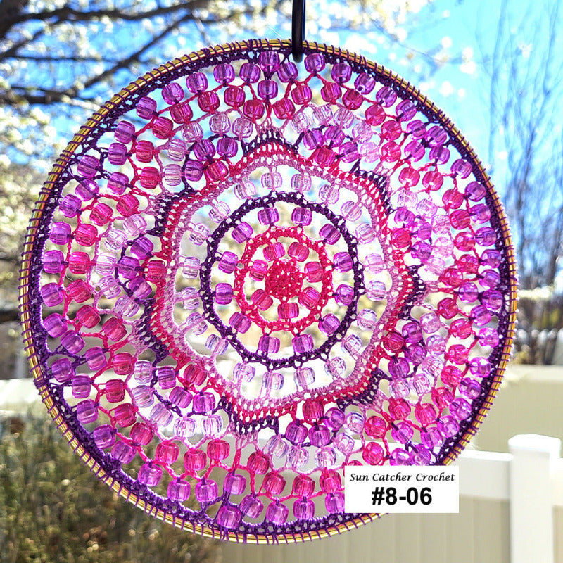 Circular beaded sun catcher with pink and purple colors hanging outdoors.