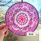 Handmade sun catcher with pink and purple spiral pattern held outdoors.