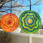 Two colorful circular decorations hanging outdoors with a blue sky and tree branches in the background.