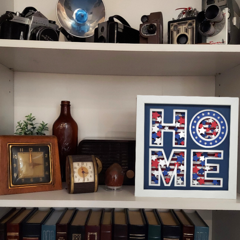 Shelf with vintage cameras, decorative bottles, clocks, and a framed 'HOME' sign.