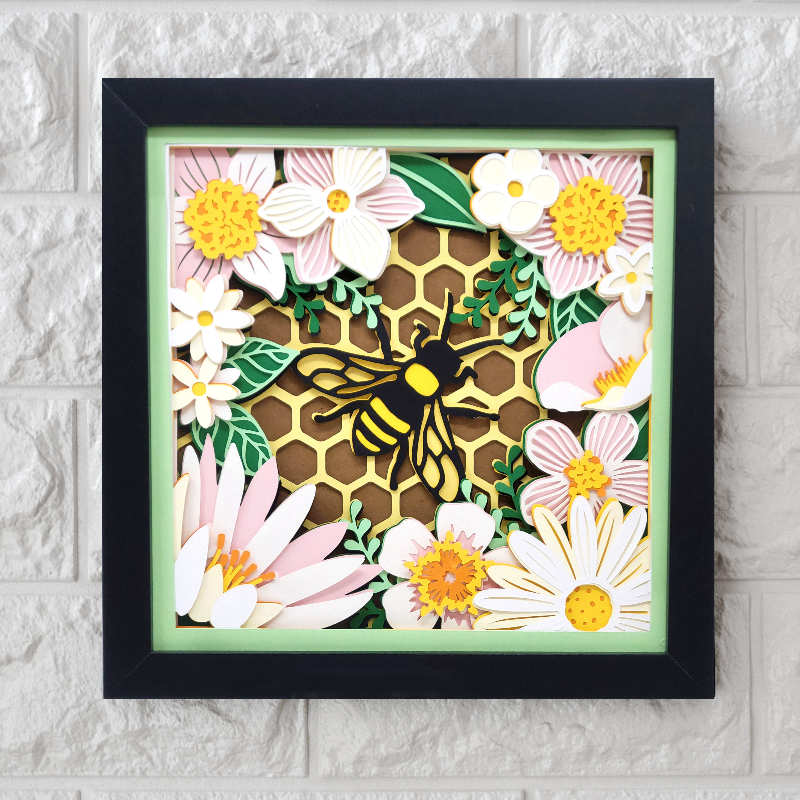 Framed artwork with a bee and floral design on a textured wall.