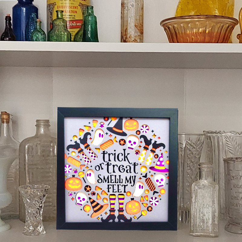 Framed Halloween-themed artwork with colorful design on a shelf with decorative bottles and items.