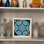 Framed blue and white geometric design on a shelf with vintage bottles and glassware.