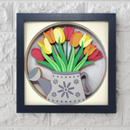 Framed artwork of colorful tulips in a watering can with a blue frame on a textured white wall.