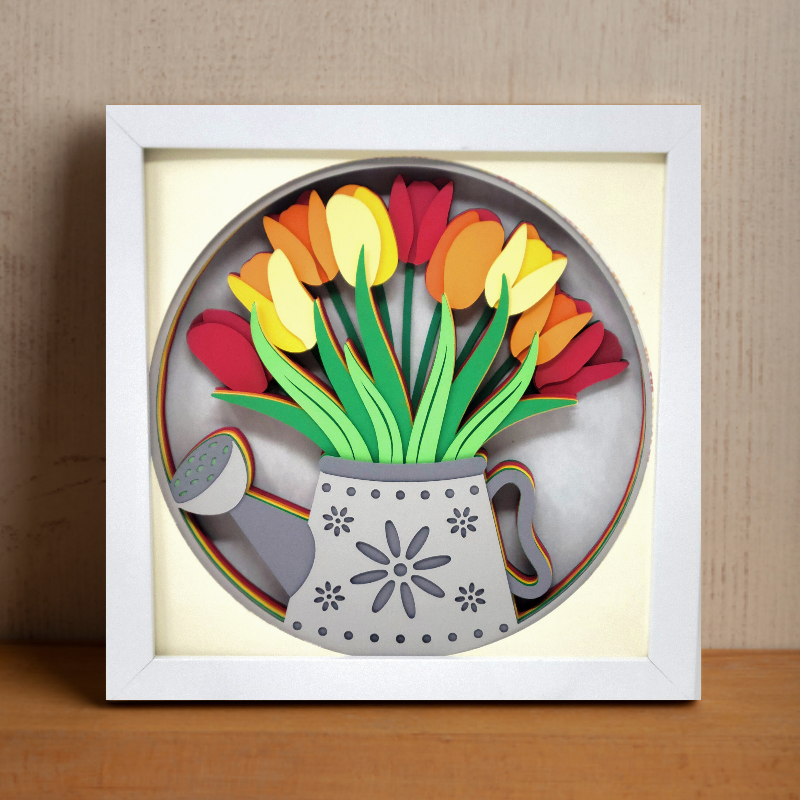 Framed artwork of tulips in a watering can on a wooden surface with a beige wall background.