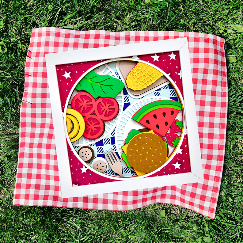Colorful toy food set on a red and white checkered blanket on grass