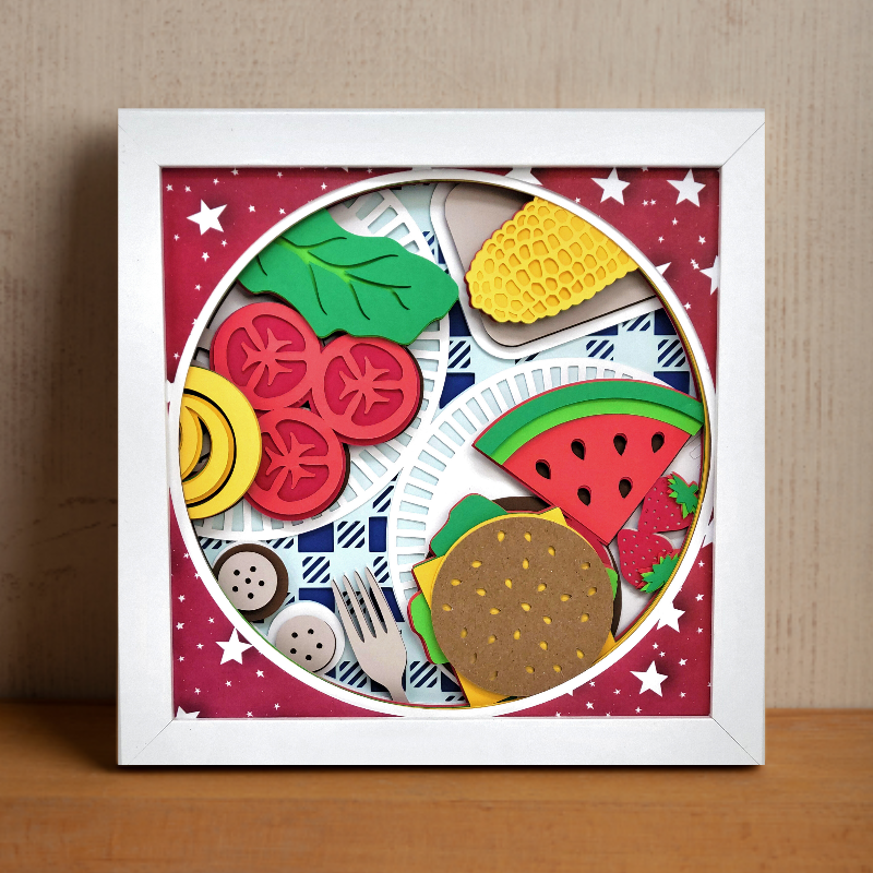Framed artwork with colorful paper cutouts of food items on a red background.