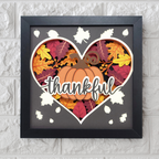 Decorative wall art with a pumpkin and leaves in a heart shape, featuring the word 'thankful'.