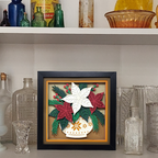 Decorative framed artwork with floral design on a shelf with vintage bottles and glassware.