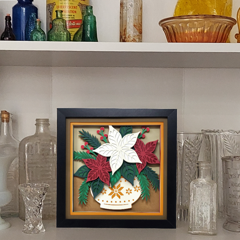 Decorative framed artwork with floral design on a shelf with vintage bottles and glassware.