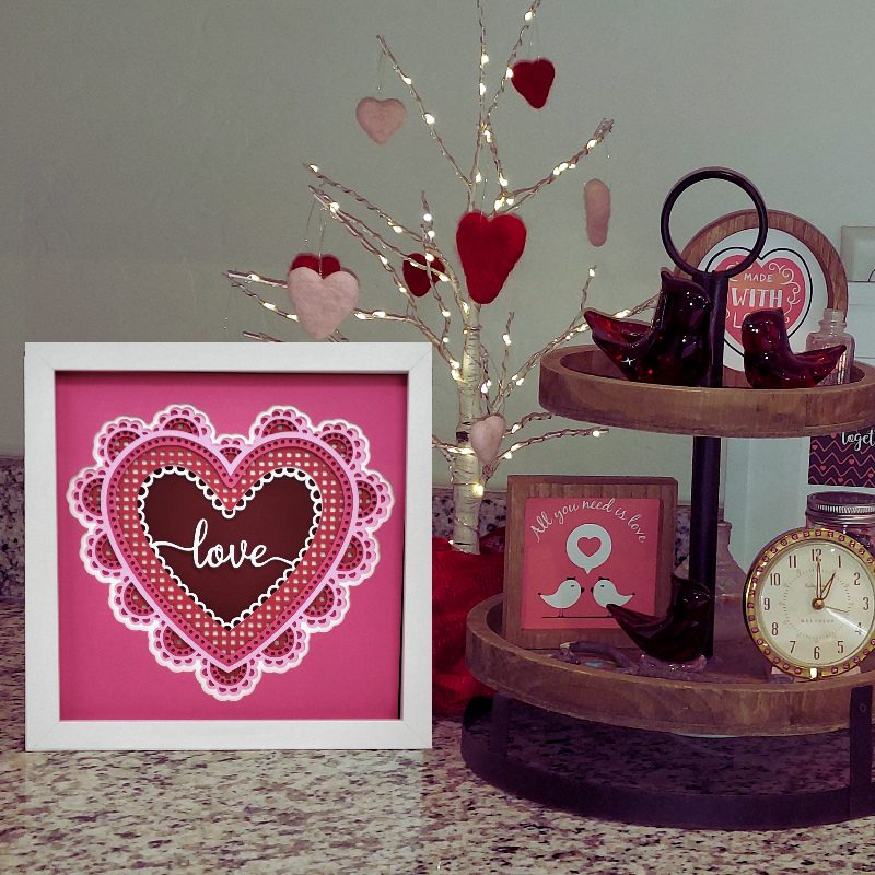 Decorative setup with a heart-themed picture frame, clock, and small tree with hearts on a table.