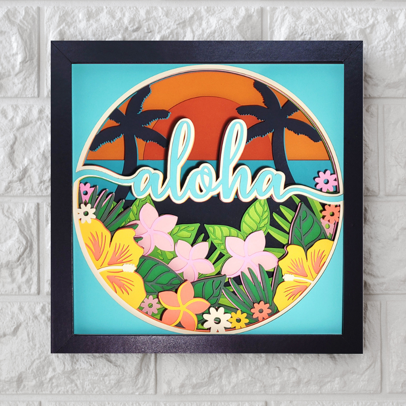 Framed artwork with 'aloha' text, tropical plants, and flowers on a white brick wall background.