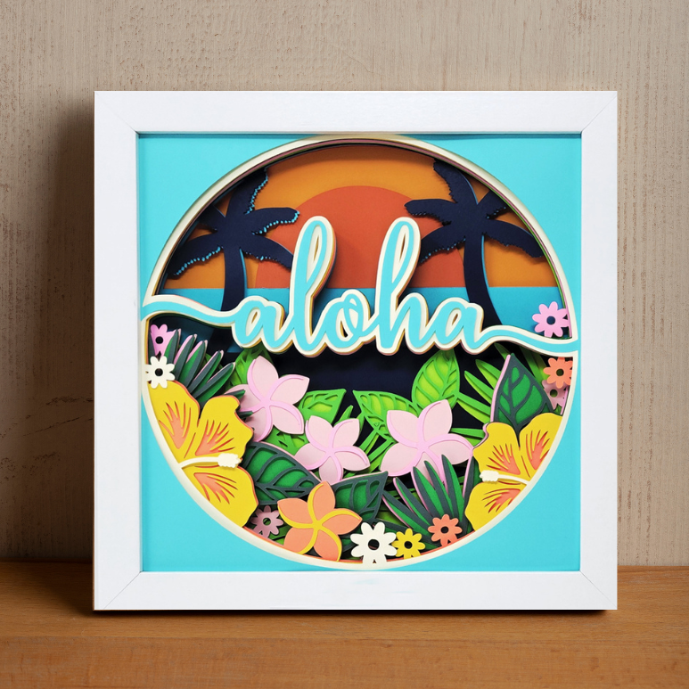 Framed artwork with 'aloha' text and tropical design on a wooden surface.