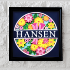 Decorative wall art with colorful flowers and the name 'Hansen' on a white brick background