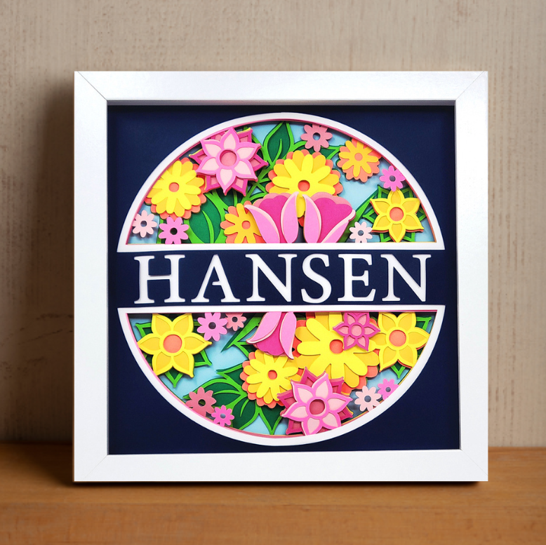 Framed artwork with colorful flowers and the name 'Hansen' on a dark blue background.