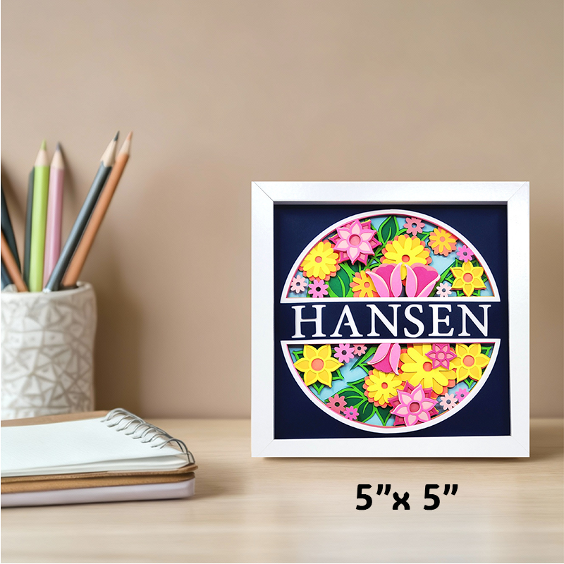 Framed decorative sign with floral design and 'HANSEN' text on a desk with stationery items.