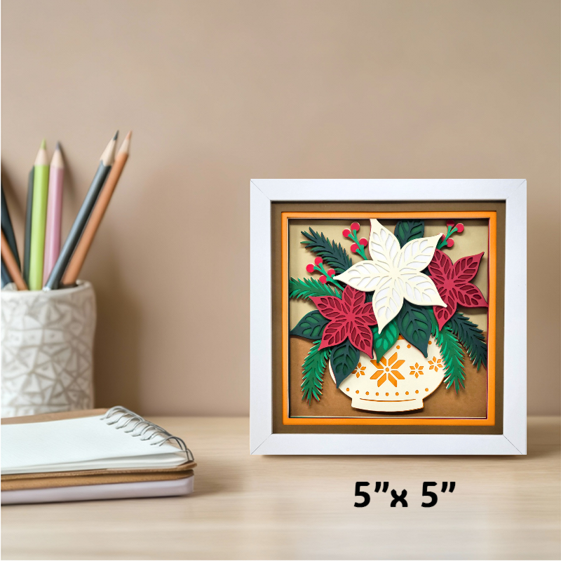 Framed decorative piece with poinsettias and a vase on a desk with stationery items.