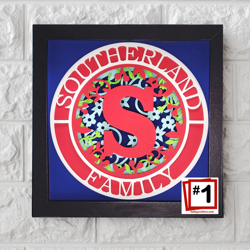 Decorative wall art with a red 'S' and floral patterns on a blue background, framed in black.