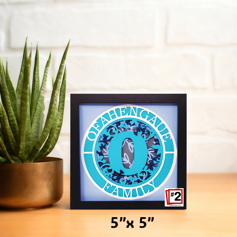Framed decorative item with a blue circle design on a wooden surface next to a plant.