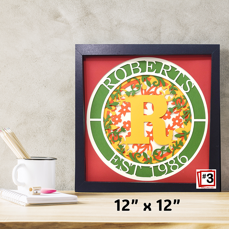 Decorative framed piece with 'ROBERTS' and 'R' design on a red background, placed on a surface.