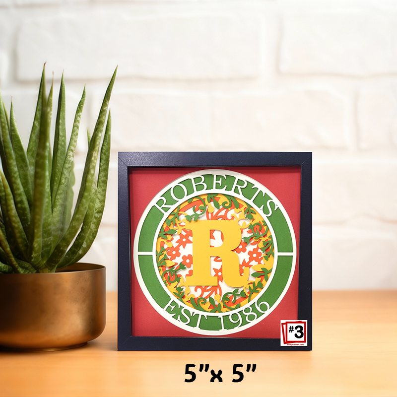 Framed decorative item with 'ROBERTS' and '1986' on a table with a plant in the background