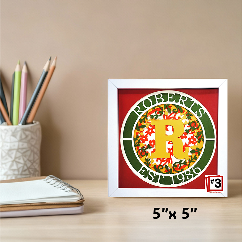 Framed decorative item with a letter 'R' on a red background, placed on a desk with stationery items.