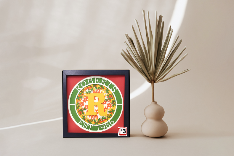 Framed artwork with a colorful design on a white surface next to a decorative vase.