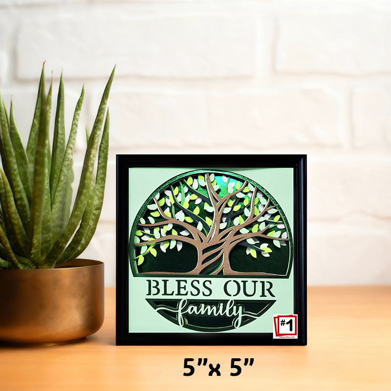 Framed artwork with a tree design and 'Bless our family' text on a light green background, next to a potted plant.