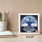 Framed artwork with a tree design and 'Barlow Family' text on a desk with stationery items.