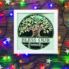 Decorative wall art with a tree design and 'Bless Our Family' text, surrounded by colorful string lights on a wooden background.